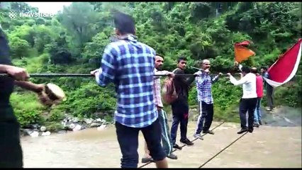 Devotees and villagers balance on rope to cross flooded river
