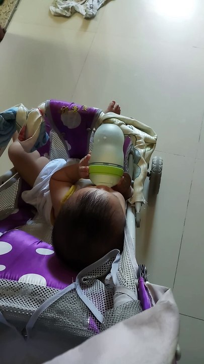 An 8-month-old baby holds a bottle of super cute milk