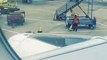 Airport worker flips a cone onto another, dabs, and then dives onto a baggage trolley