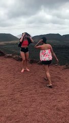 Two girls jump for the camera and one loses her sliders into a volcano