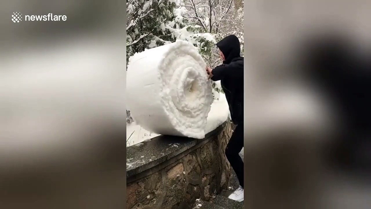 Man 'folds' snow on top of a wall into giant snowball