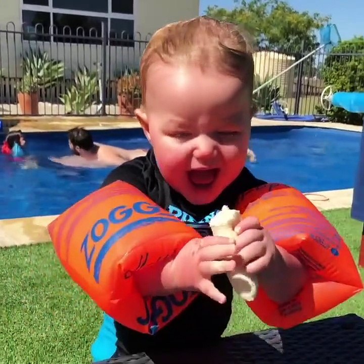 Un enfant veut manger une banane avec des brassards de natation