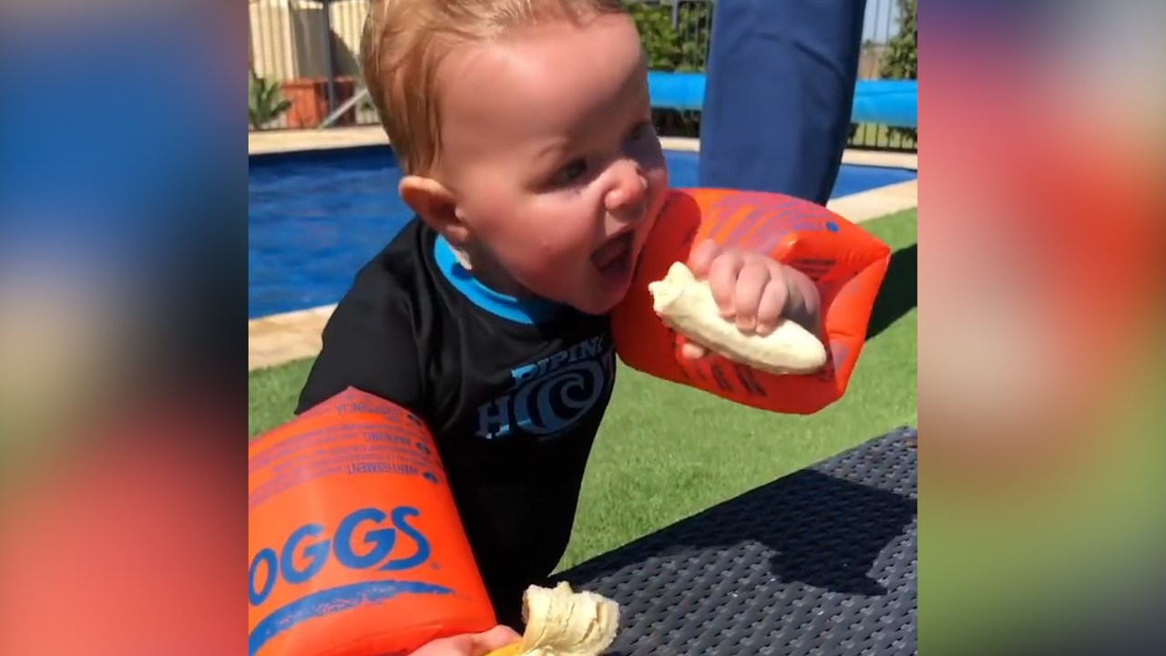 Un enfant veut manger une banane mais ses brassards de natation l'en empêche !