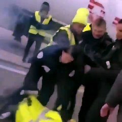 Un policier met une grenade lacrymogène dans la veste d’un gilet jaune.