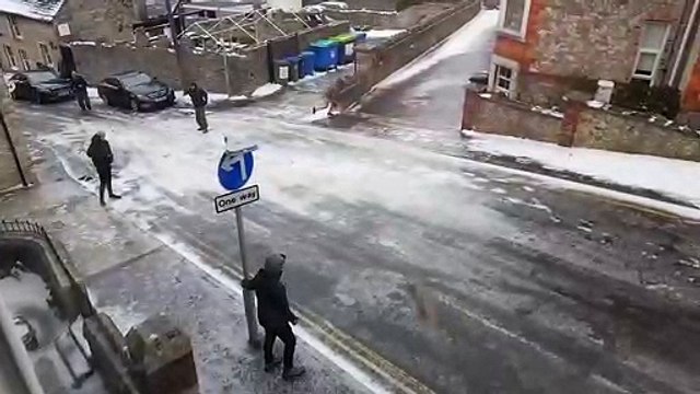 Un groupe d'hommes essayent en tout moyen de monter une route glissante