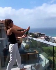 Une blonde veut ouvrir une bouteille de champagne depuis son balcon