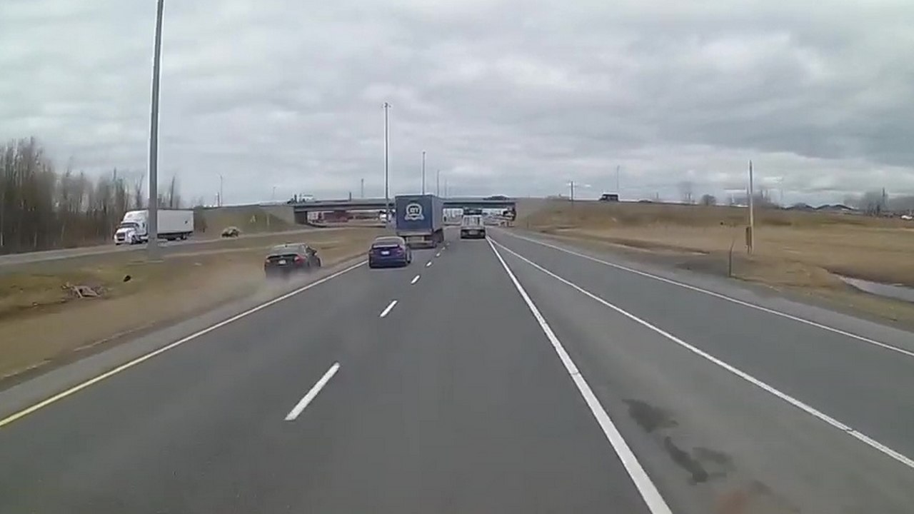 Un automobiliste impatient passe par l'herbe pour doubler deux camions sur l'autoroute