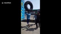 Man perfectly balances a huge tyre on his head as he climbs on the roof of a bus