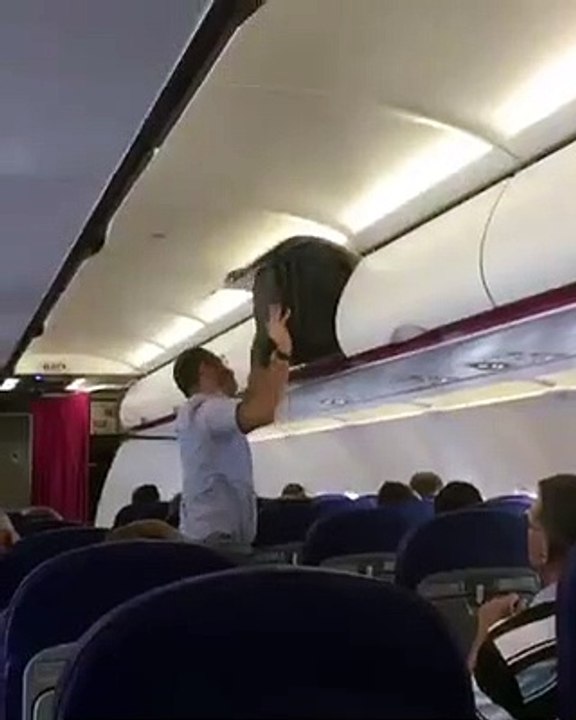 Régis essaye de mettre une valise dans un compartiment