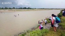 Children walk across a flooding river to attend school