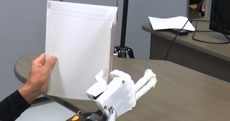 El sujeto amputado sostiene un cuaderno usando la prótesis de mano mioeléctrica con control de sinergia muscular