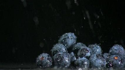 Water falling on blueberries on black background