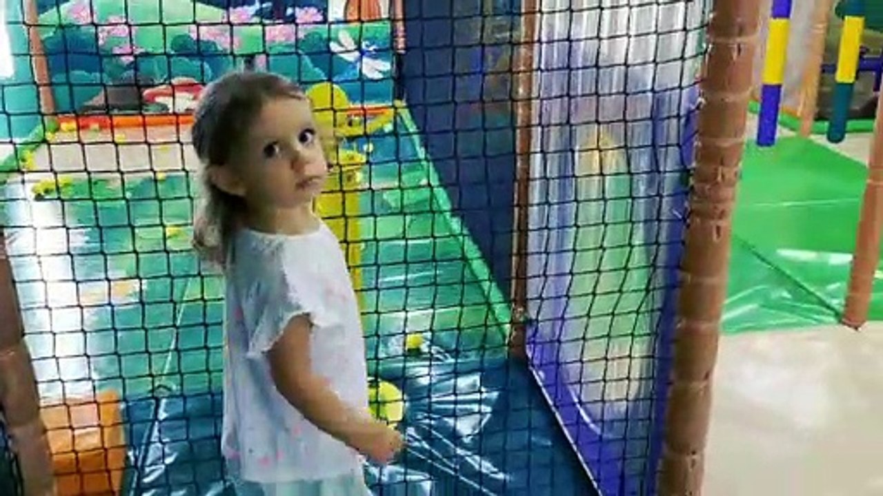 Little Mia playing in indoor playground for kids on slide and shooting gun. Kids entertainment