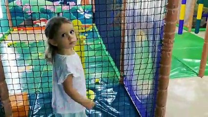 Little Mia playing in indoor playground for kids on slide and shooting gun. Kids entertainment