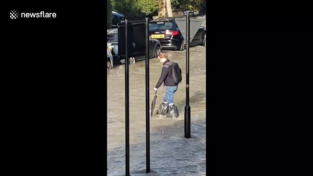 Man ties bin bags around legs as he wades through London floodwater