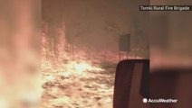 Firetruck drives through road surrounded by raging wildfire