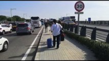 Viajeros caminan por la carretera arrastrando maletas hacia El Prat