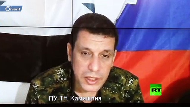 قائد ميليشيا قسد يتحدث وخلفه علما نظام الأسد والاحتلال الروسي