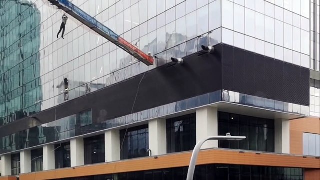 La nacelle de laveurs de vitres se balance au vent contre le gratte ciel !