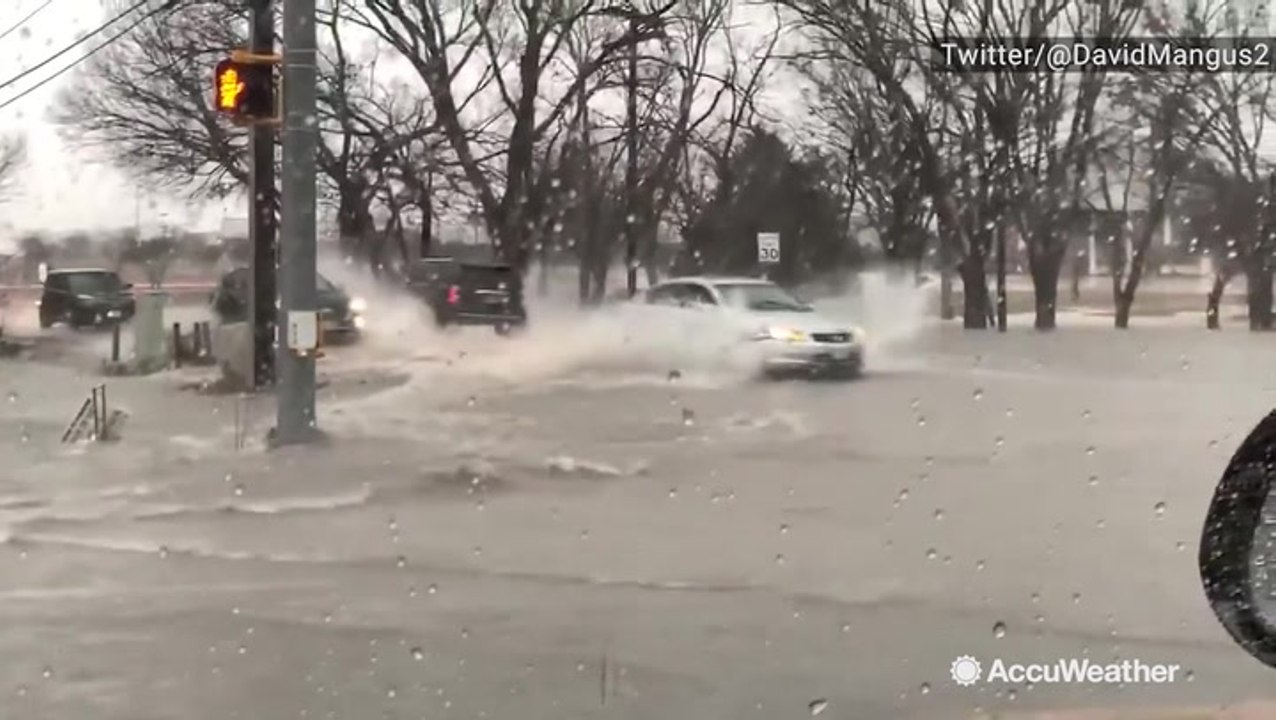 Waves of water crash against cars driving through flooded streets