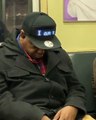 Un dormeur dans un métro porte une casquette avec un message défilant.