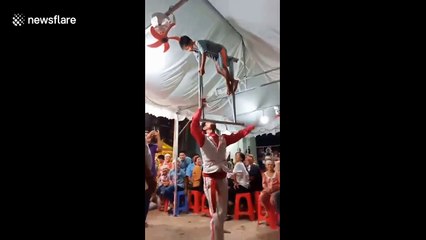 Vietnamese street act dances while balancing metal bar with child on top on his mouth
