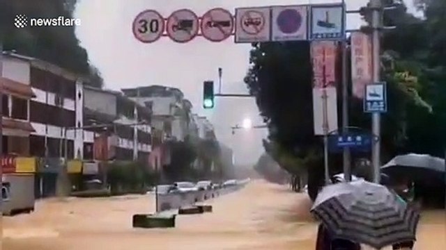 Chinese pedestrians hold hands and stand behind pole to avoid being washed away by flash floods