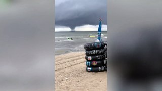Spinning water tornado towers over people playing on beach