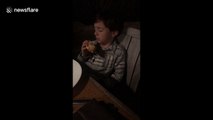 Bleary-eyed boy bites into pizza while trying to sleep
