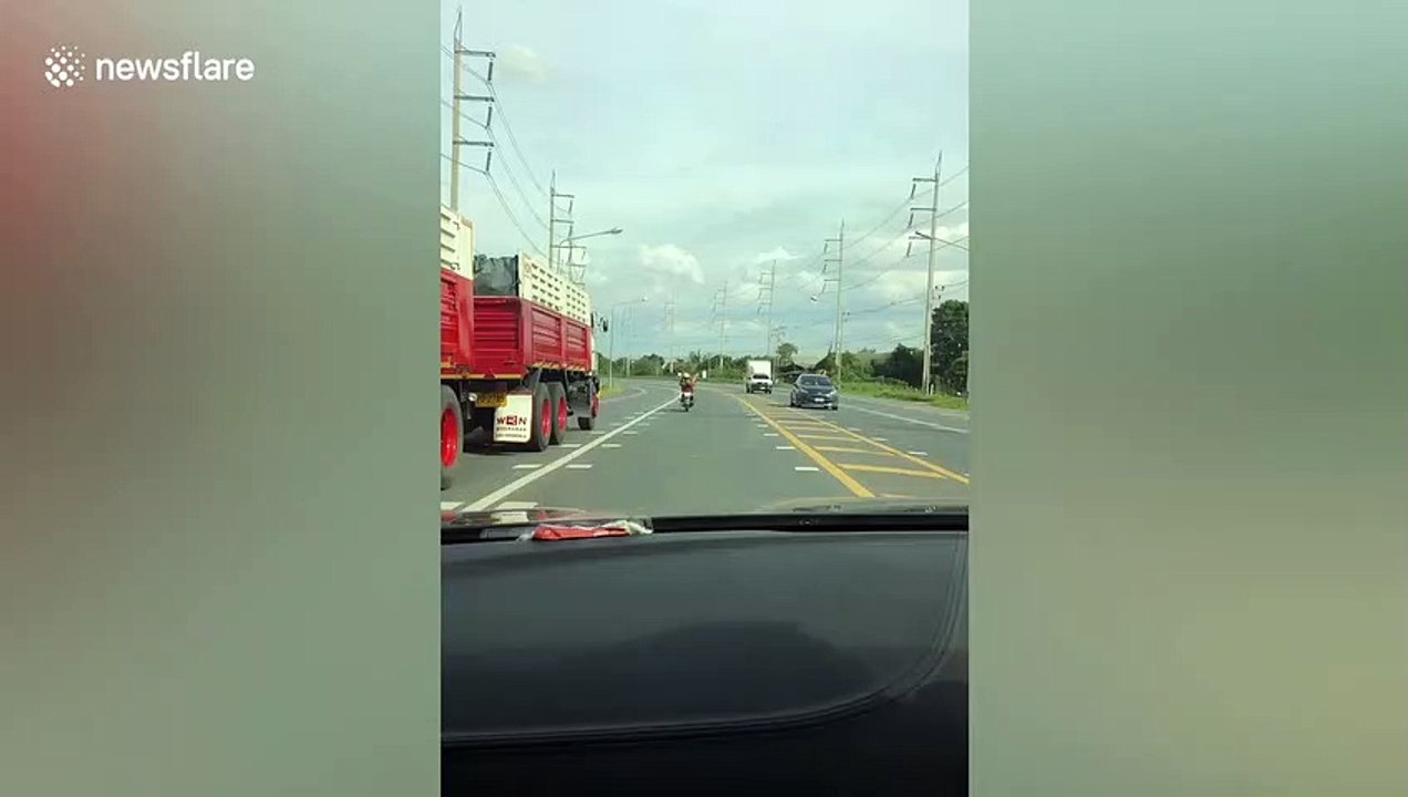 Daredevil motorcyclist lays down to steer with his foot while driving along Thai road