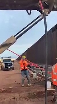 Un migrant escalade le mur à la frontière USA Mexique sous les yeux des ouvriers