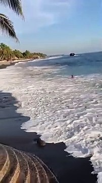 Un surfeur ravagé par une grosse vague en bord de plage