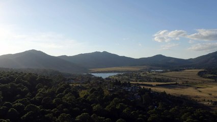 Panorama around a forest with a lake, a village and mountains