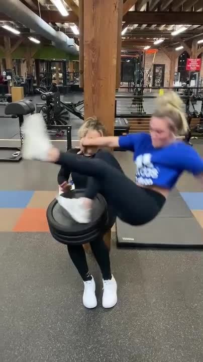 Woman Tries One Legged Jump On Weight Plates Stacked On Persons Lap