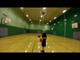 Man Dribbles Two Basketballs While Balancing Third in Middle of Vertical Hoop Over His Chin