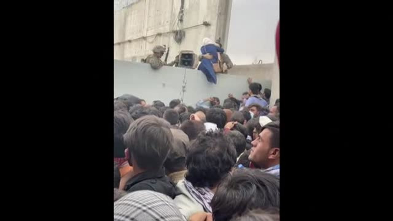 Soldados estadounidenses ayudan a una mujer afgana a saltar el muro del aeropuerto de Kabul