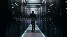 Following_Shot_of_IT_Engineer_Walking_Through_Data_Center_Corridor_with_Rows_of_Rack_Servers._Opens_Laptop.