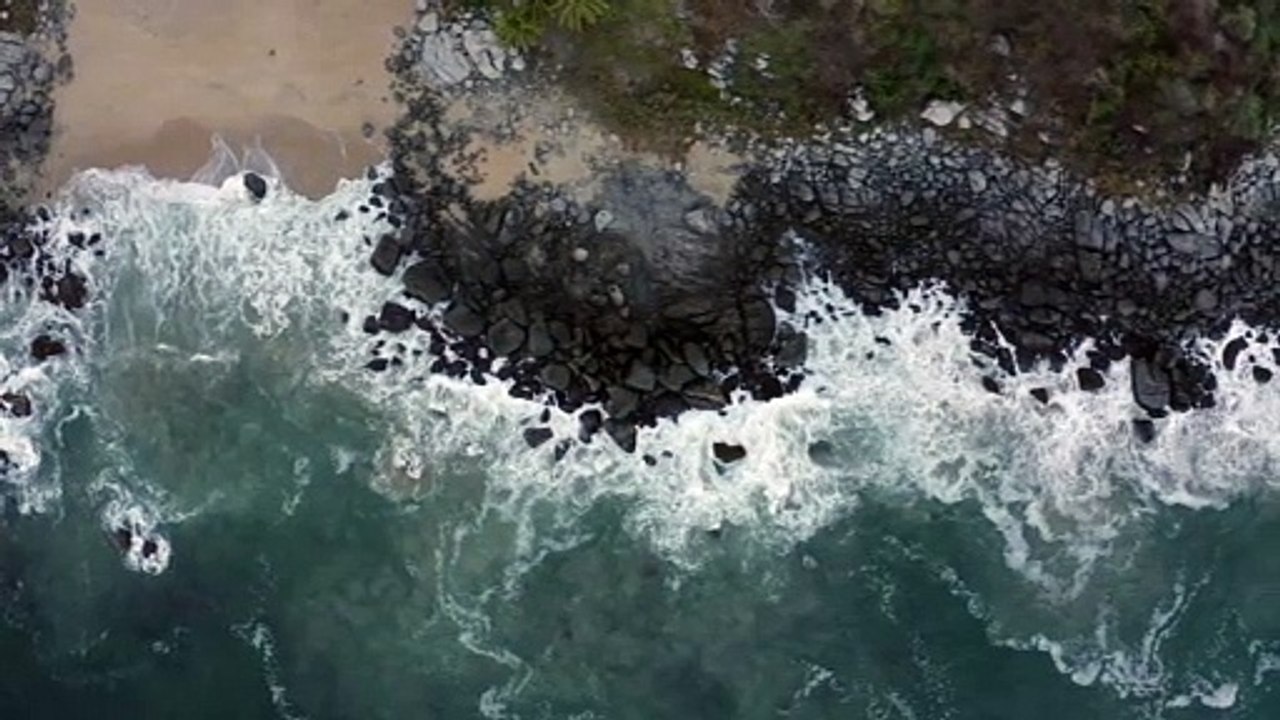 Top aerial shot of seashore with black shore rocks being hit by waves