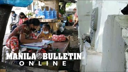 Candles and flowers vendor assists her daughters in answering their modules while waiting for customers in Davao City’s Roman Catholic Cemetery