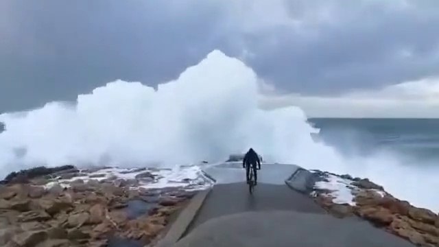 Un cycliste se rapproche un peu trop près du bord de mer pendant la tempête