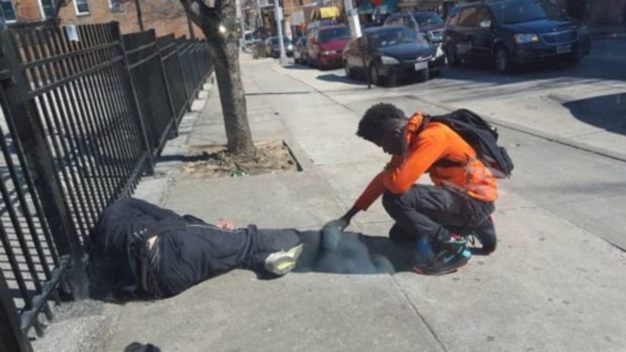 Ein Polizist fotografiert einen Jugendlichen, der den Fuß eines Obdachlosen hält und für ihn betet