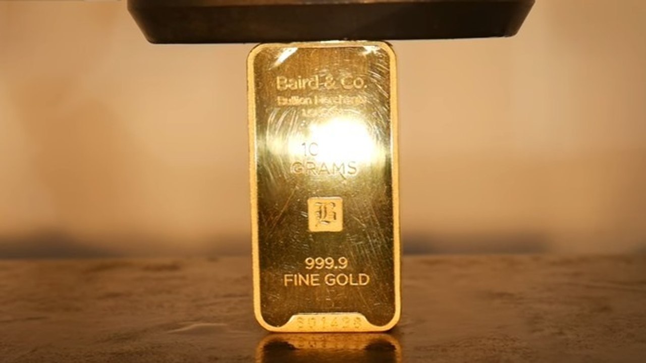 Ein Mann zerquetscht einen Goldbarren mit einer hydraulischen Presse