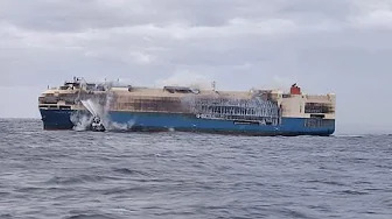 Tug boats spray water on burning ship carrying Porsches, Bentleys