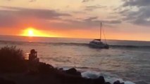 Un catamaran se fait emporter par une vague sur les rochers