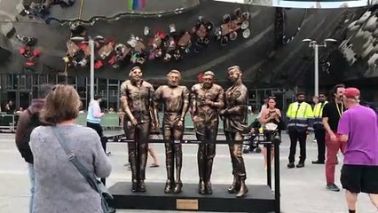 The 'four lads in jeans' who rose to internet fame when their photo was turned into a meme have posed next to a statue in the spot the pic was taken