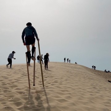 Julien grimpe la dune du Pilat sur ses échasses landaises