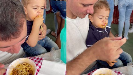 Toddler puts his fast, little hands to work while eating noodles with dad