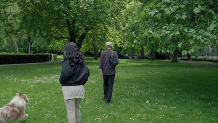 A Couple Is Walking With An Australian Shepherd In The Park.