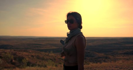 A Woman Walks On The Edge Of a Hill With a Weapon.