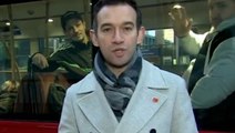 Waving bus passengers stop behind BBC journalist during live report on strike disruption